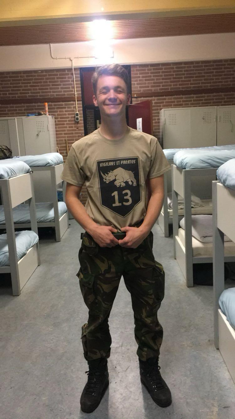 Young Sjakie Minet smiling in army uniform in a barracks dormitory, bunk beds behind him