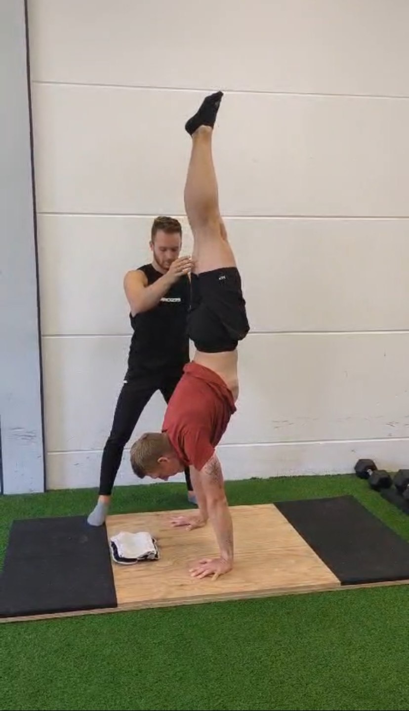 Sjakie Minet coaching an athlete in a handstand, correcting his hip position by hand